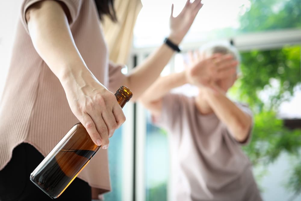 Caregiver abusing elderly woman in nursing home while holding an alcohol bottle, highlighting violence and alcohol addiction issues.